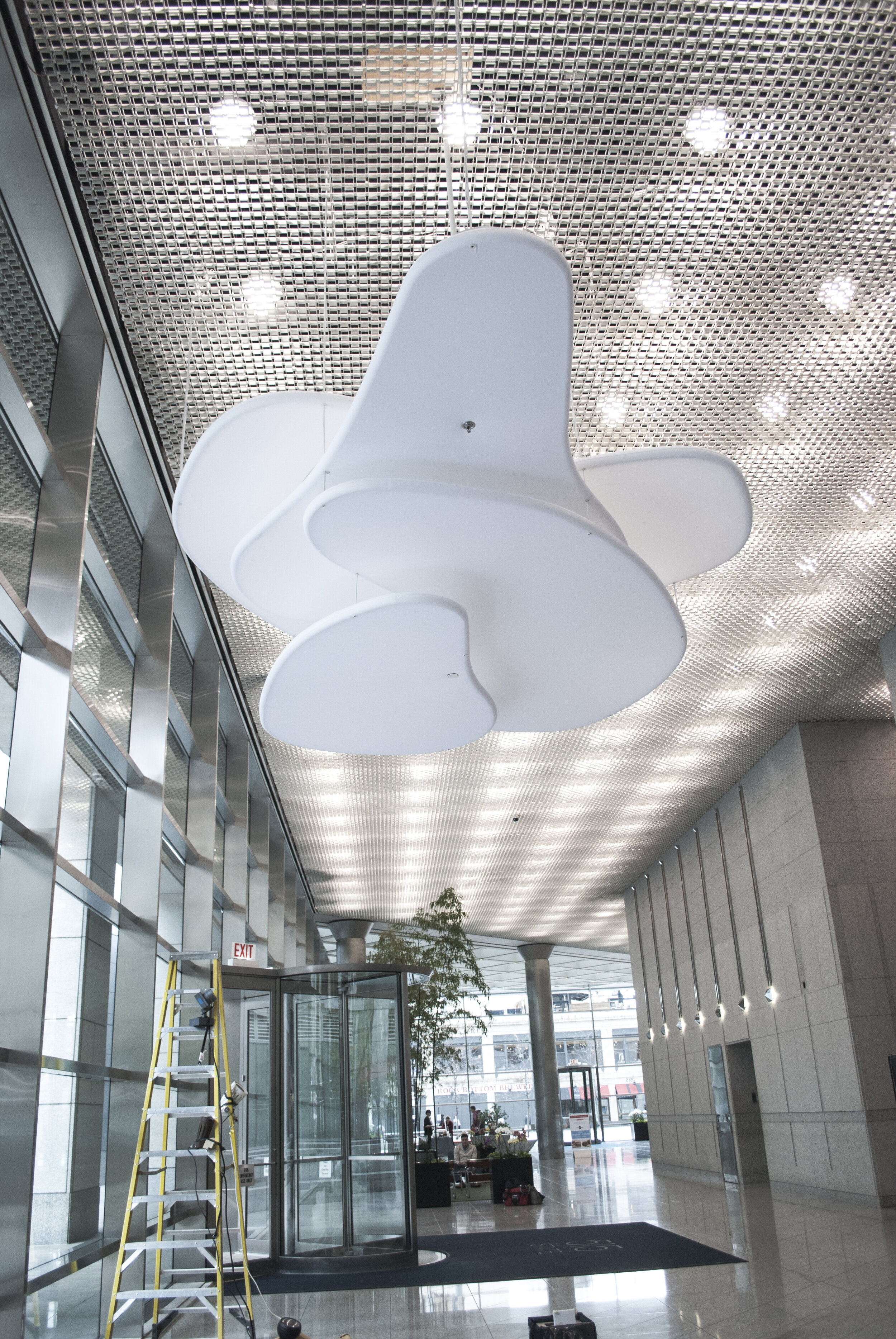 An abstract light fixtures hangs from a lobby. A ladder shows it was freshly installed.