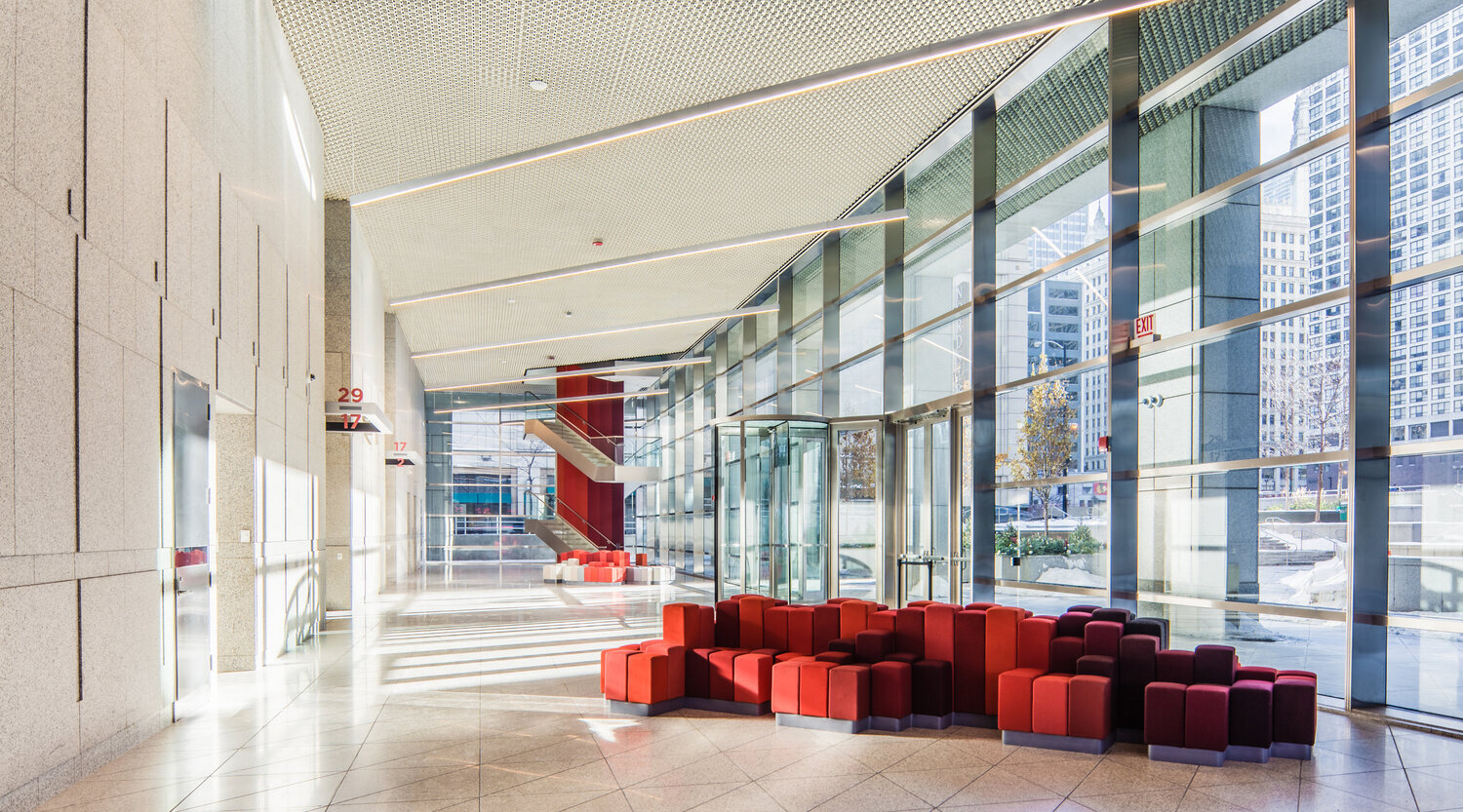 The well lit, bright lobby with natural light, wrap-around stairs, and red minimalist seating.
