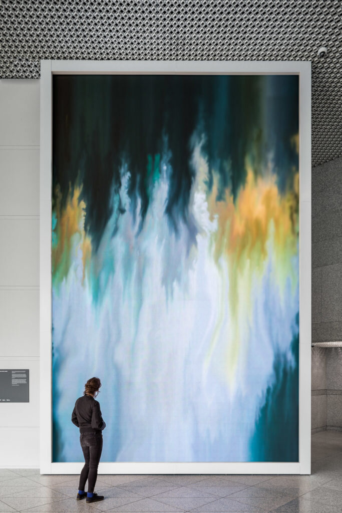 A person looks up at the large digital display of moving abstract art in the lobby.