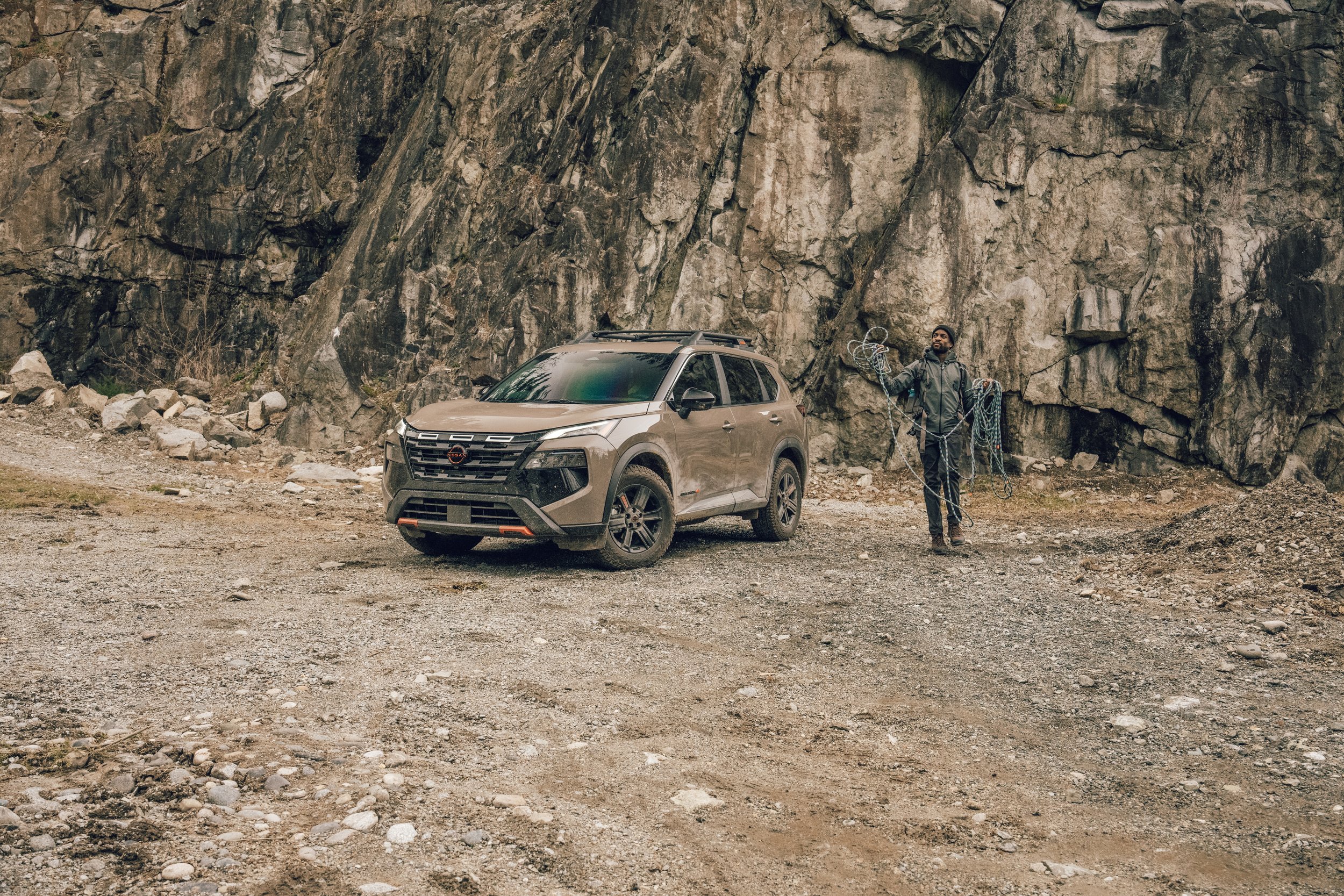 A man holding climbing ropes standing next to a car near a large rocky cliff