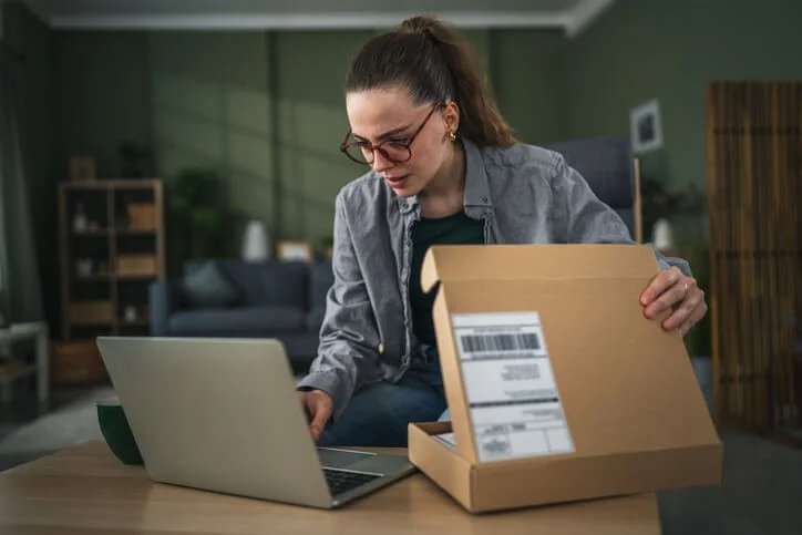 Remote employee preparing a company laptop for return using a standardized shipping box during offboarding.