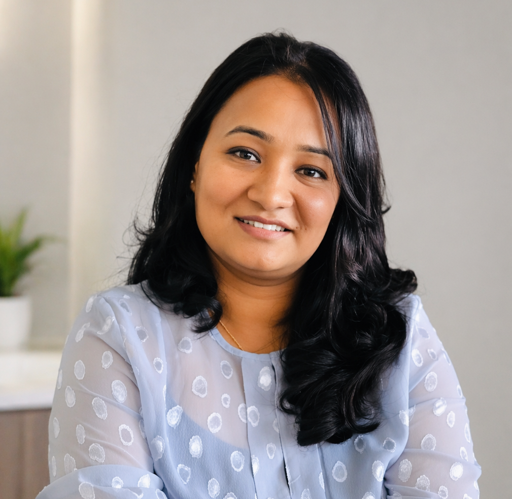 A woman with long black hair and a light blue polka dot blouse smiling at the camera.