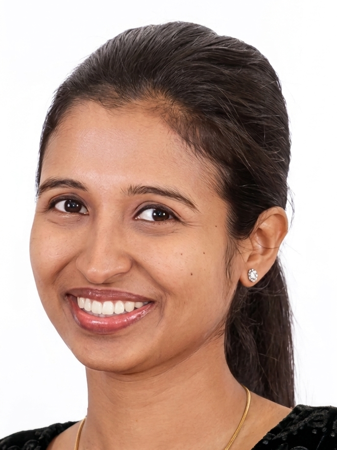 Close-up portrait of a young woman with dark hair, smiling, wearing earrings and a black top, against a white background.