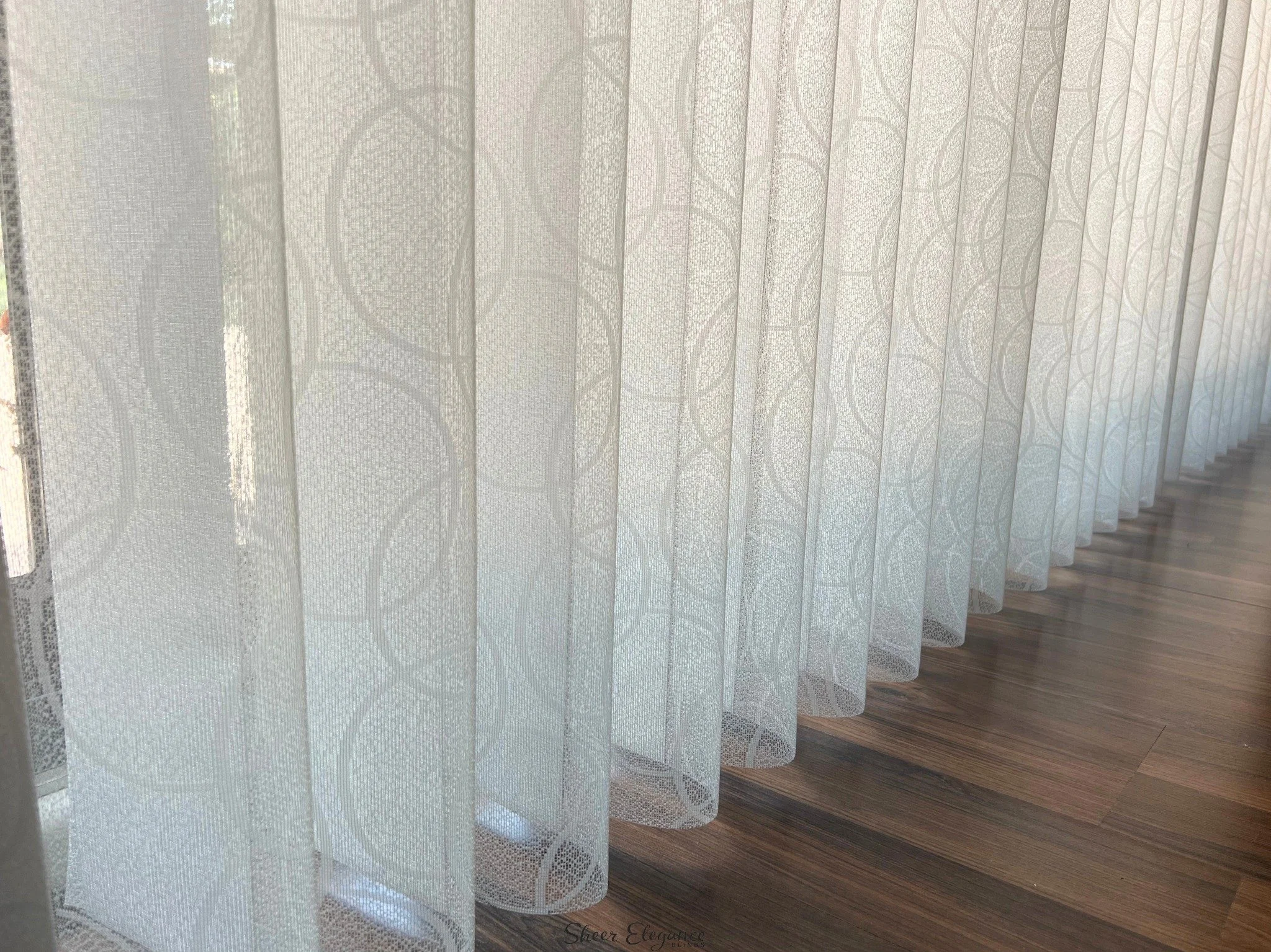 Close-up of layered lace curtains with floral patterns at a window, with a wooden floor visible underneath.