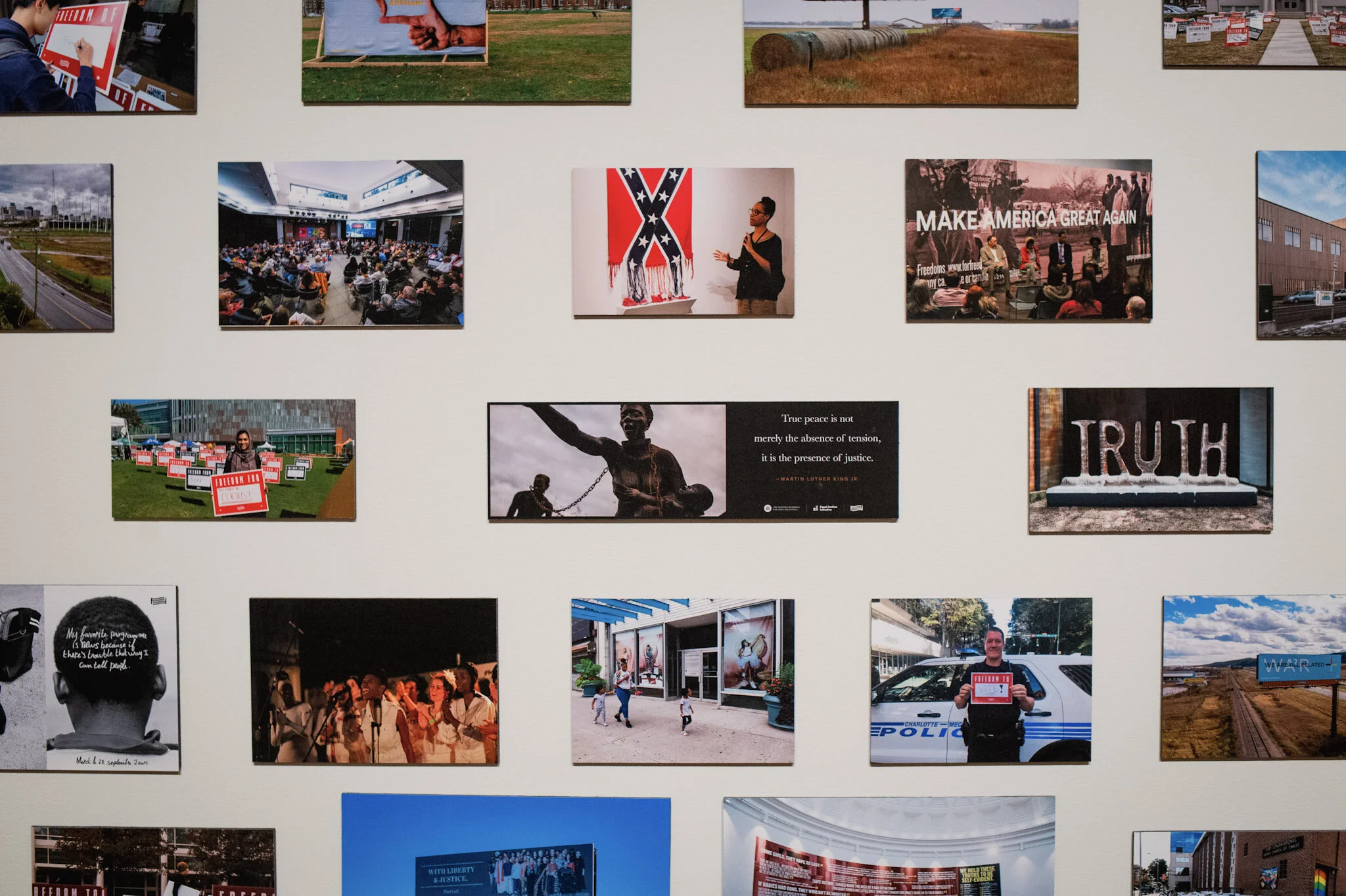 A wall display of various photographs related to social activism, protests, and community events. The photos include people holding signs, a speaker at a rally, artwork, and cityscapes.