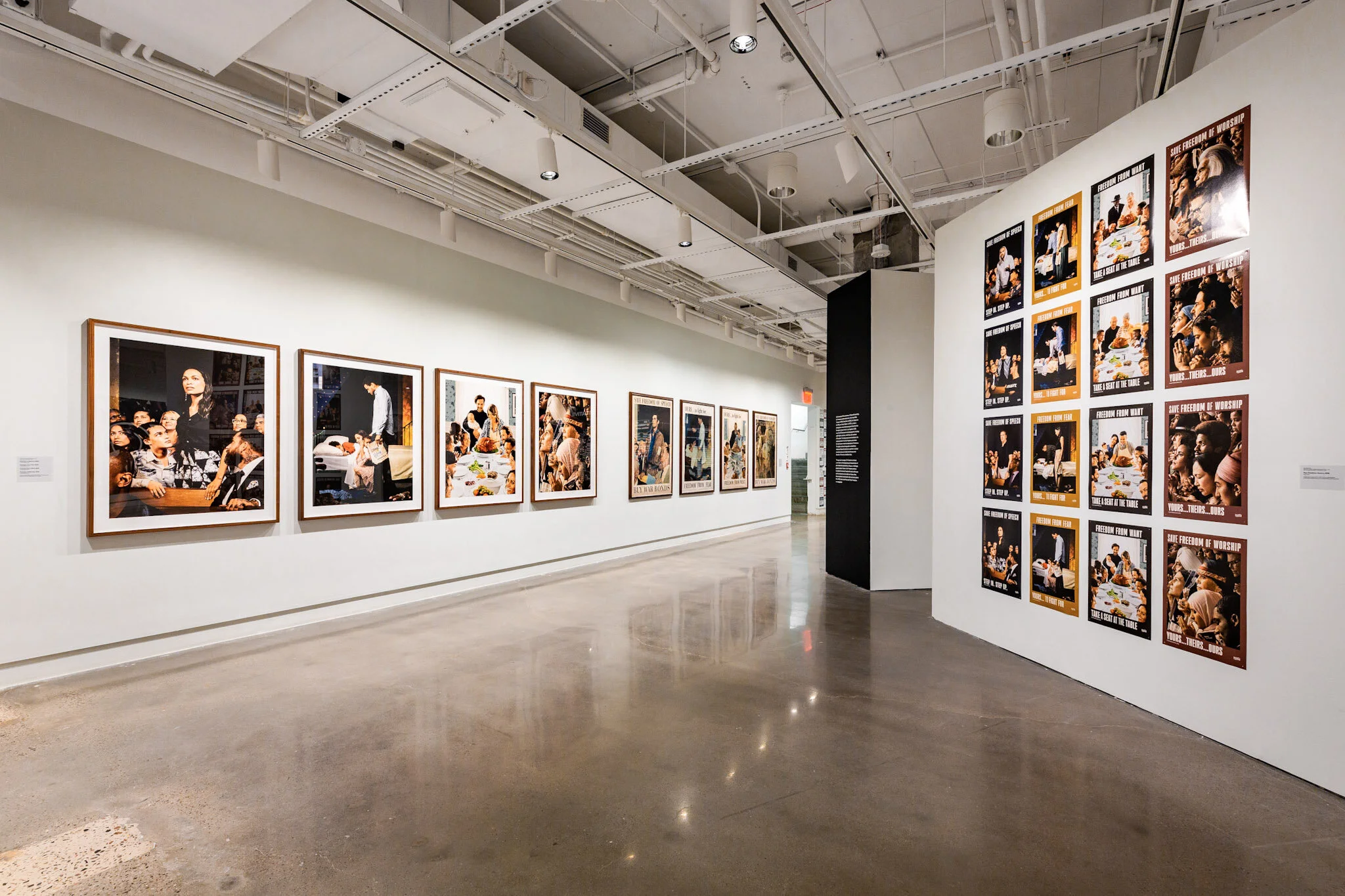 An art gallery featuring framed photographs on white walls. The photographs depict people in various social settings, including a group of children gathered around a table, and other individuals engaged in conversations. The gallery space has a polis