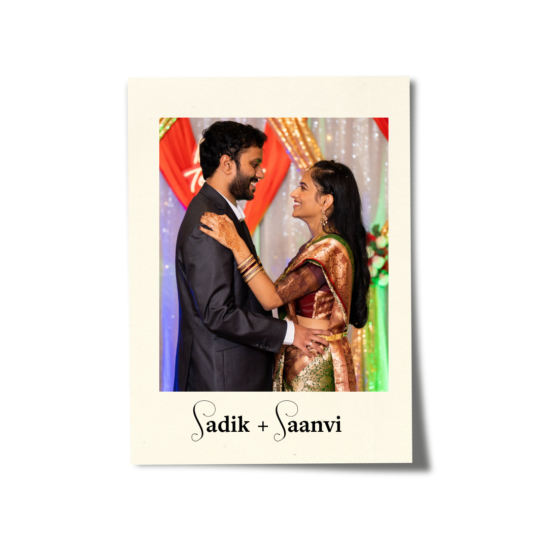 A couple in traditional Indian attire smiling and looking at each other during a celebration, with colorful decorations in the background. The text below reads 'Sadik + Saanvi'.