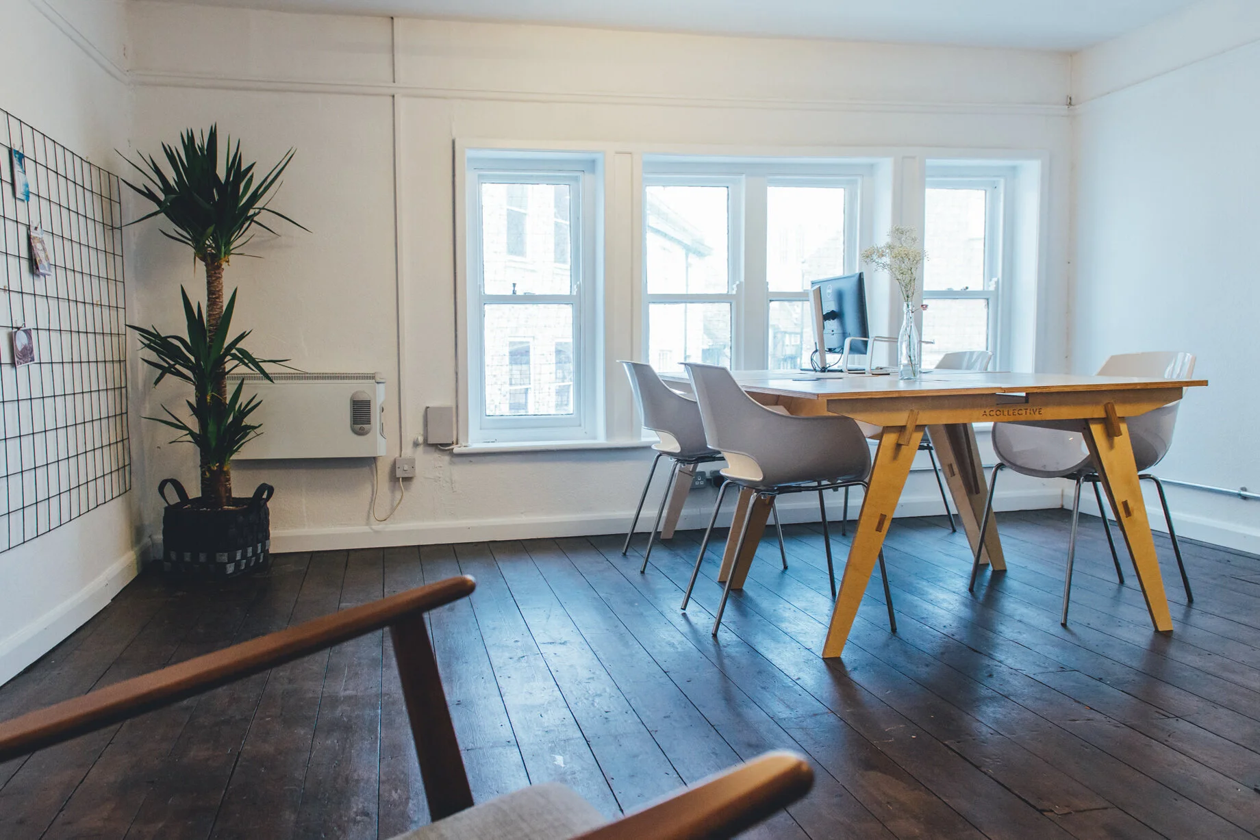 York city centre office – four person - with a wooden table and white chairs, a plant, open windows, and a computer monitor