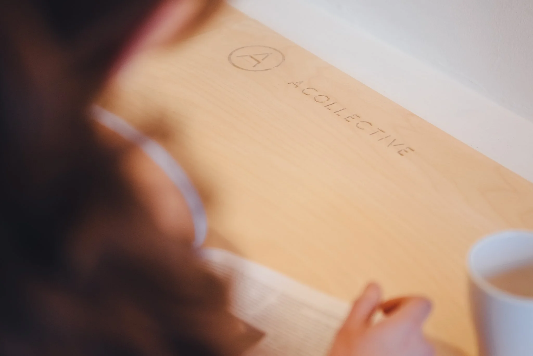 A person's hand with a ring is seen resting on a wooden surface with the words 'COLLECTIVE' and a logo engraved on it.
