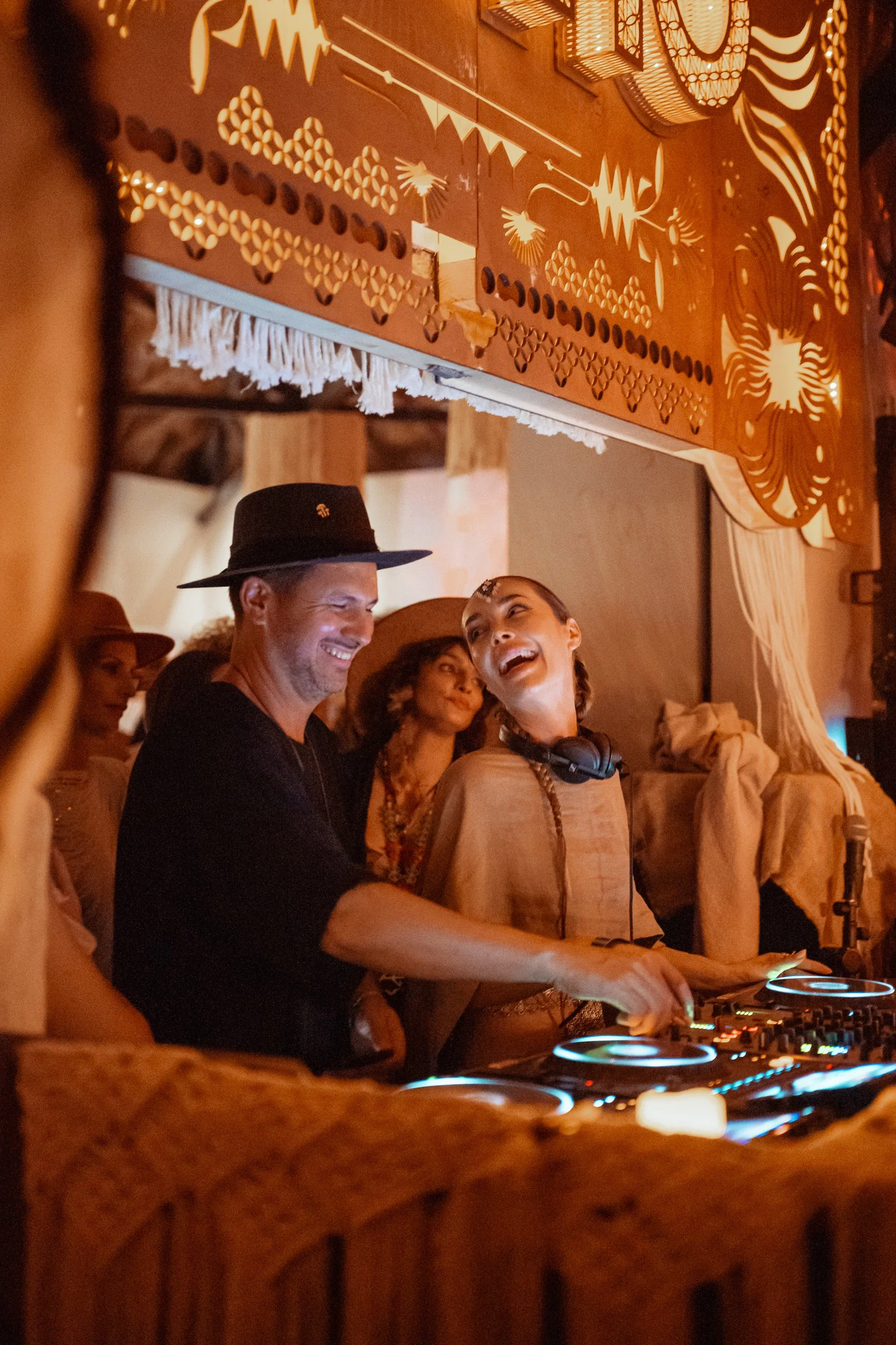 Group of people enjoying a DJ performance at a cozy indoor event with intricate wall art and warm lighting.