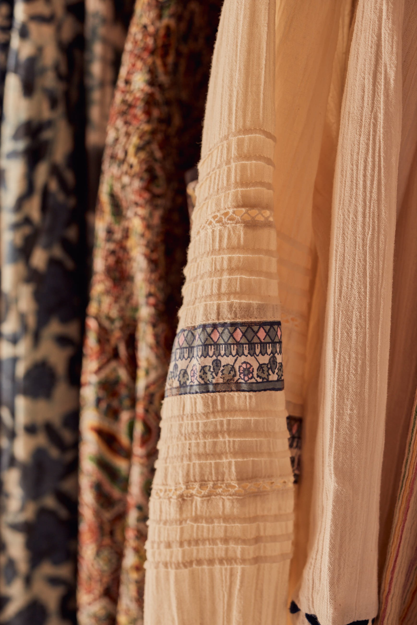 Close-up of hanging patterned and textured fabrics in a clothing store. The fabrics feature floral, geometric, and striped designs in various colors.