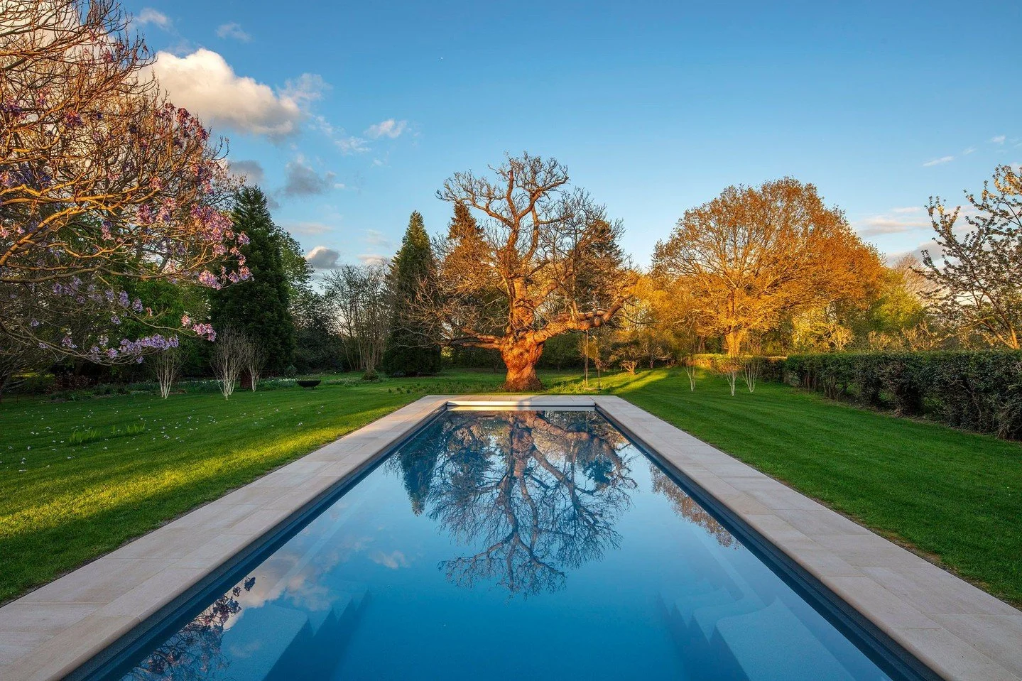Golden hour rays illuminate the beautiful tree at the far end of the swimming pool, creating a stunning reflection that resembles a painting. Haslingden Sawn copings' olive buff tones surround the swimming pool, creating a peaceful space. 

Credits:
