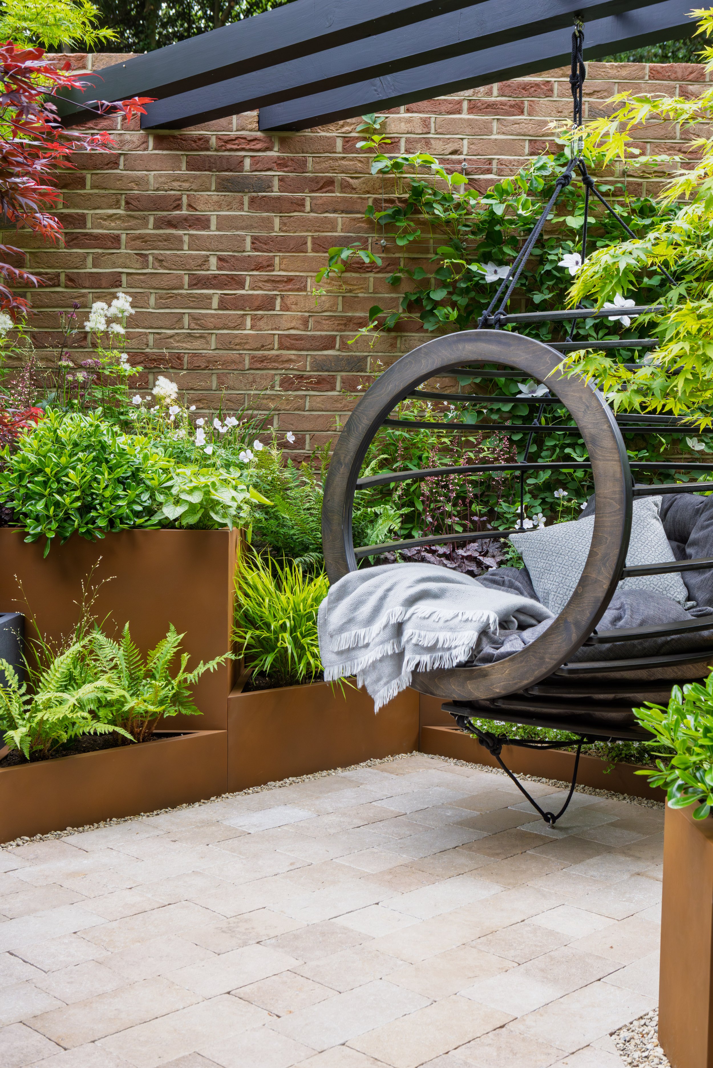 Room to breathe garden featuring a metal swing, plants and beige drivesetts and pebbles.