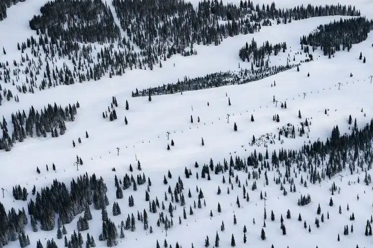 A snowy mountain landscape with evergreen trees and ski lift infrastructure.
