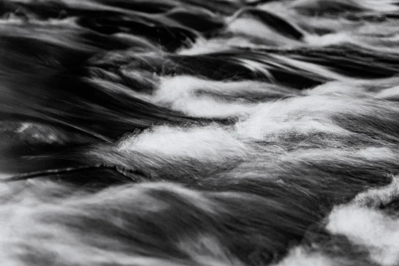 Close-up of a moving river or stream with dark water and white foam, in black and white.