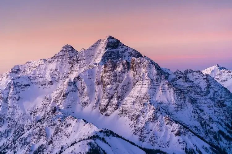 Snow-covered mountain range during sunset with pink and purple sky
