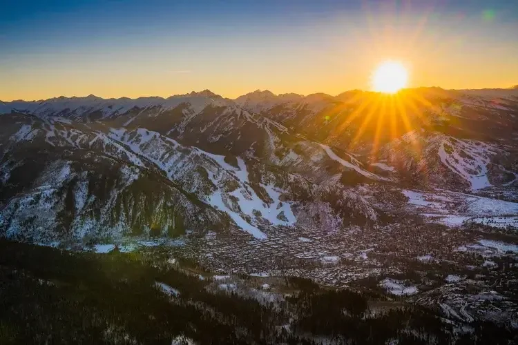 Sunset over snow-capped mountains with a valley below, illuminated by the setting sun's golden rays.
