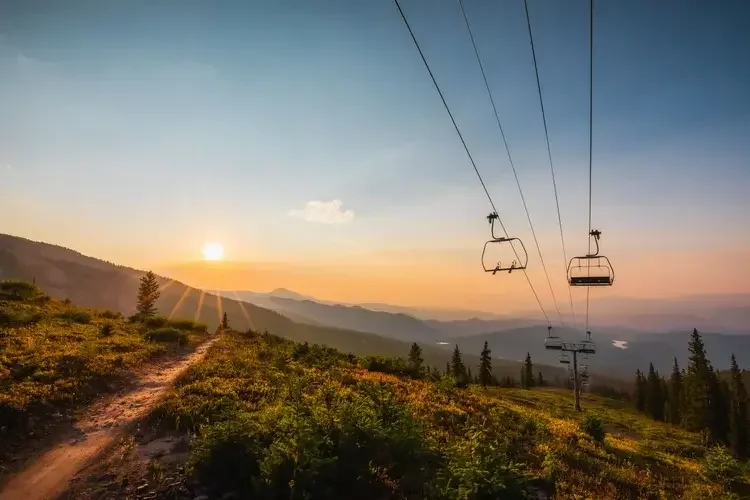 Sunset over mountain landscape with ski lift chairs in the foreground.
