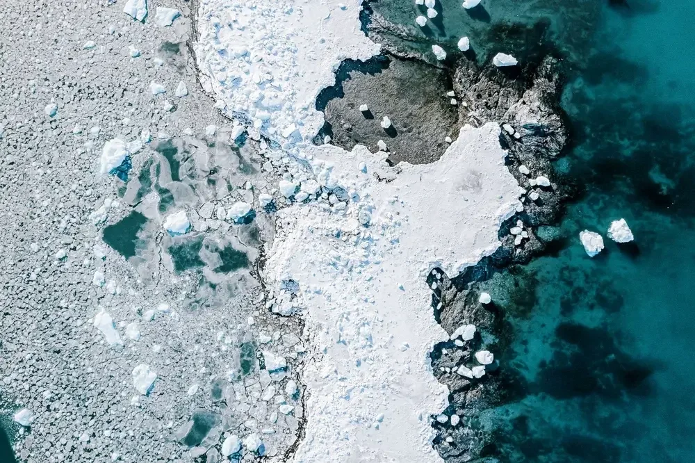 Aerial view of an icy coastline with floating ice chunks and dark blue ocean water.
