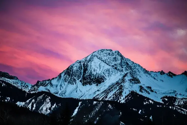Snow-covered mountain during sunset with a pink and purple sky.

