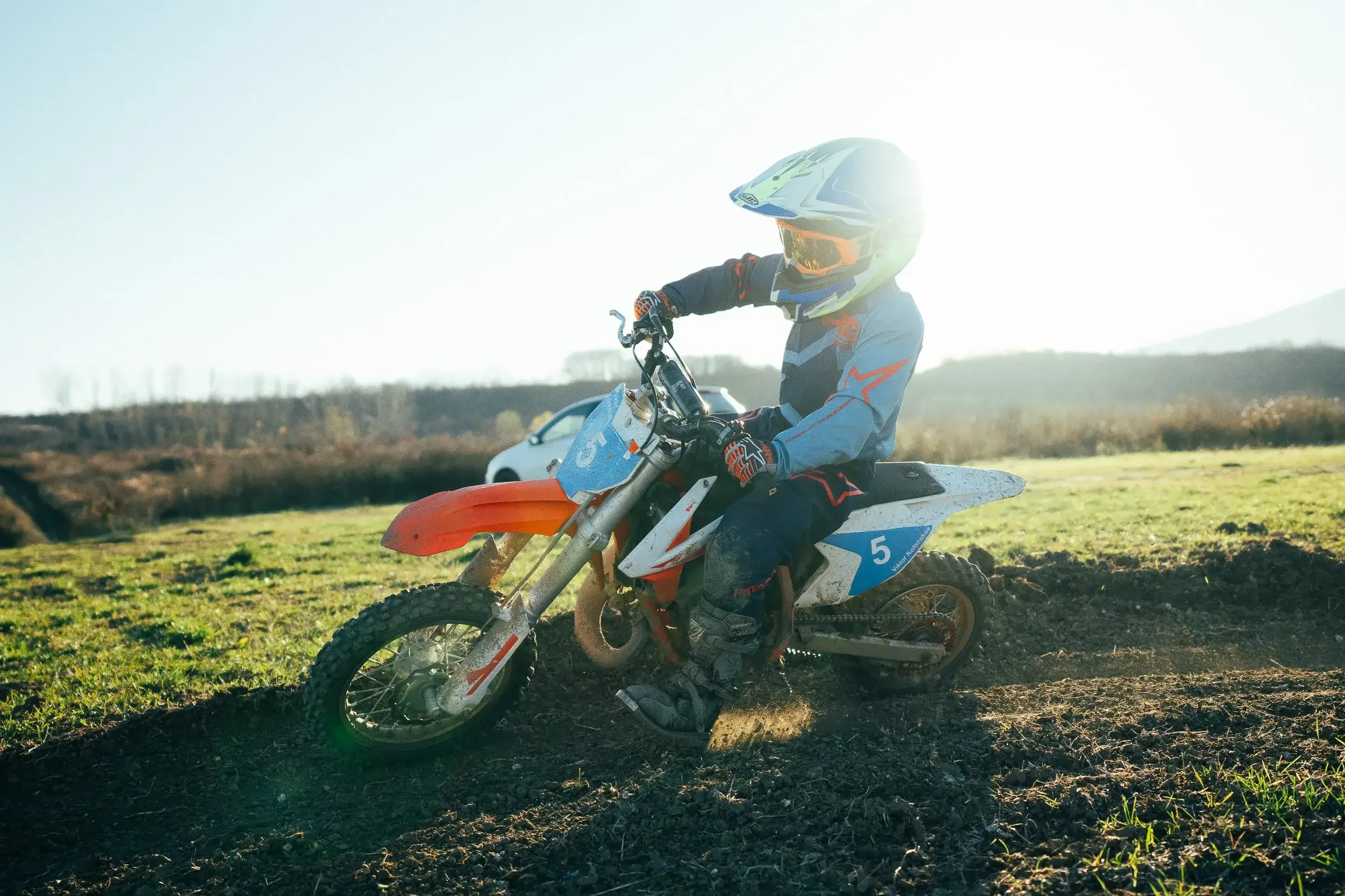 Off-road motorcycle rider wearing a helmet and protective gear riding on dirt track at sunset.
