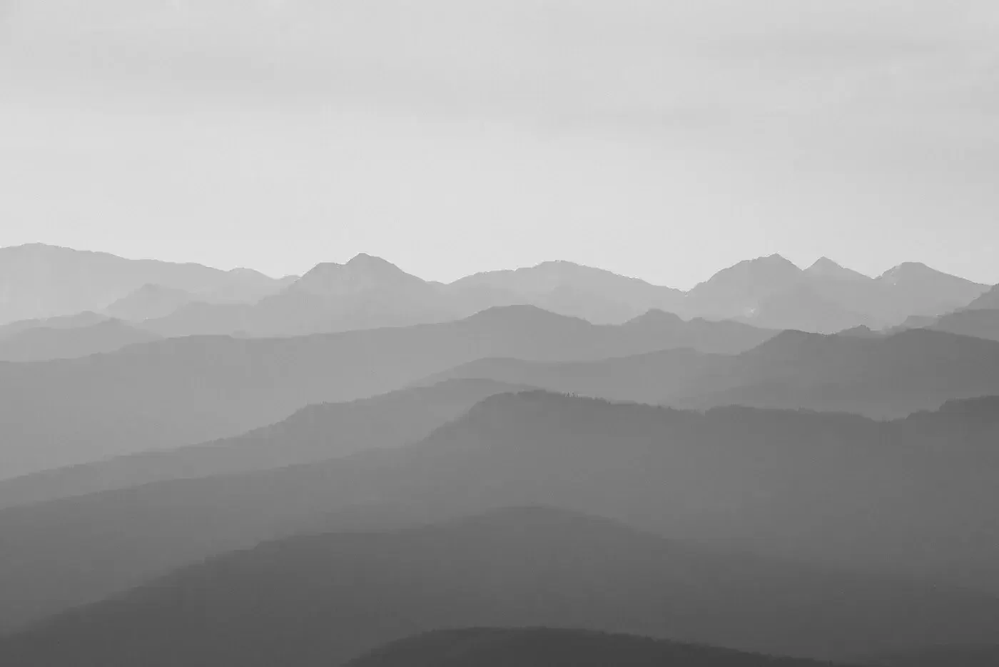 Black and white photograph of multiple mountain ranges with varying levels of fog or mist, creating a layered effect.