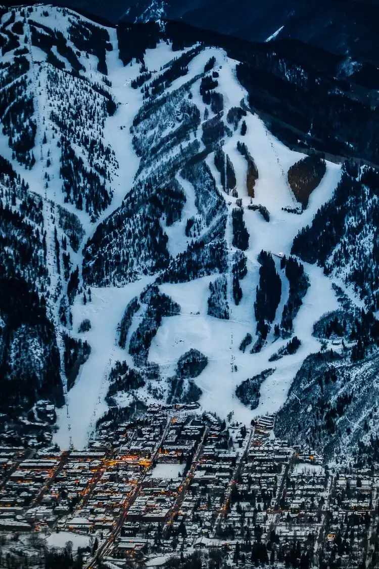 Aerial view of a snowy mountain ski resort with ski slopes and a town at the base.
