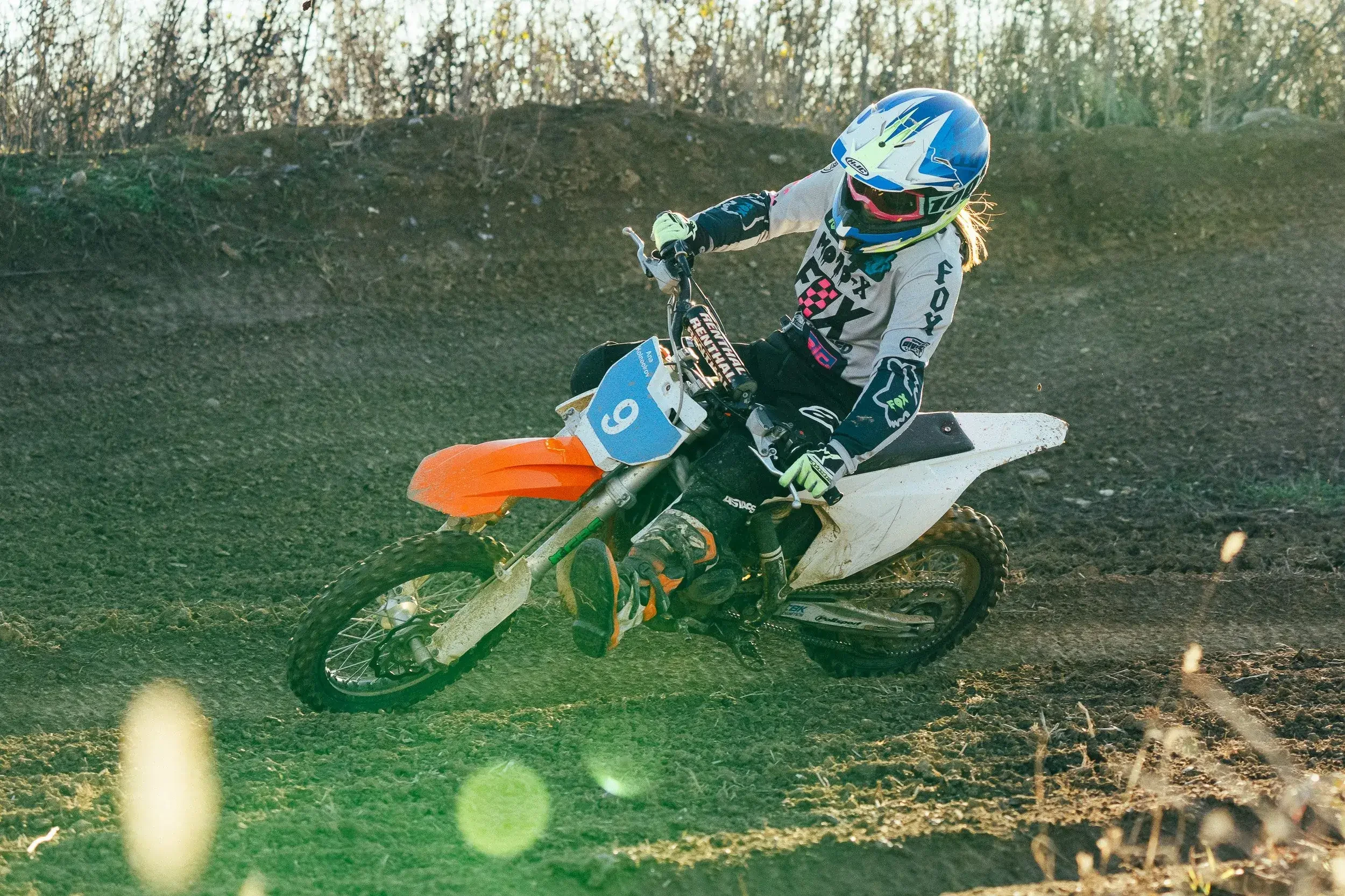 A person riding a dirt bike on a dirt track, wearing a blue helmet and protective gear.
