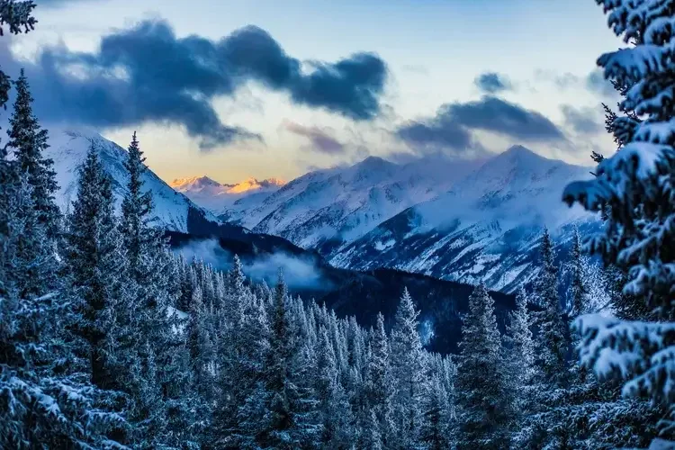 Snow-covered mountain peaks at sunset with a pinkish sky in the background.
