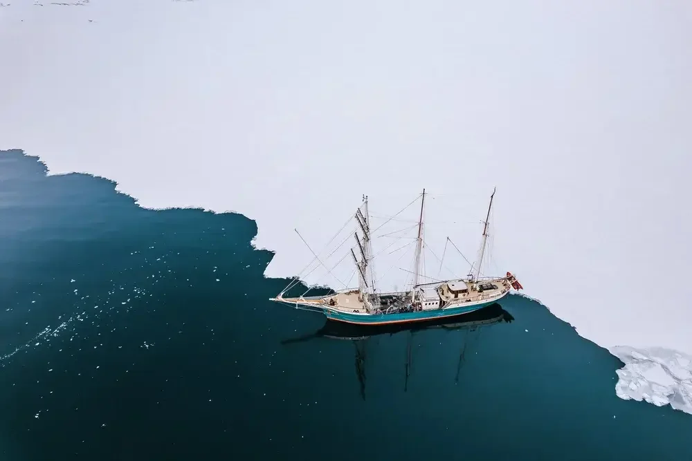 A sailboat navigating ice with a crack in the sea ice revealing open water.
