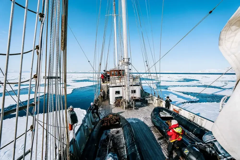 Frozen ocean with scattered ice floes, mountains in the distance, and a sunset sky with clouds.
