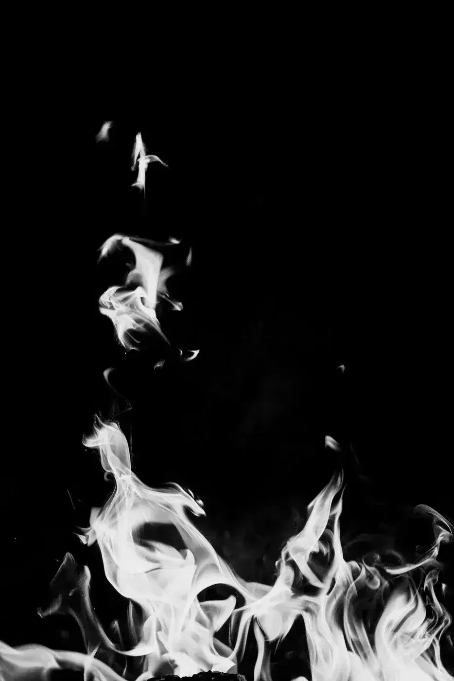 Black and white image of flames or smoke rising against a dark background.

