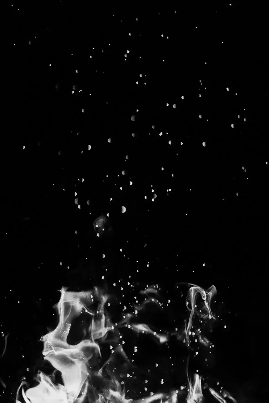 Black and white photo of sparks, smoke, and flames against a dark background.
