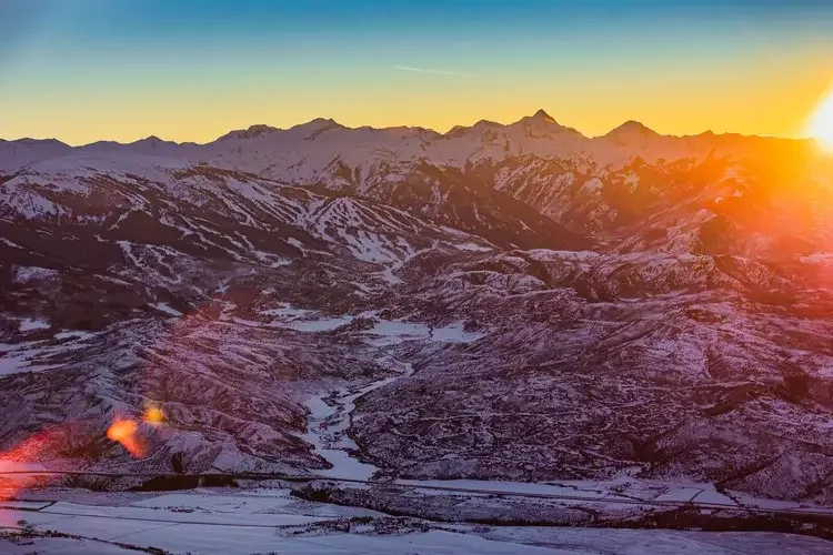 Snow-covered mountains during sunset with a clear sky and a contrail
