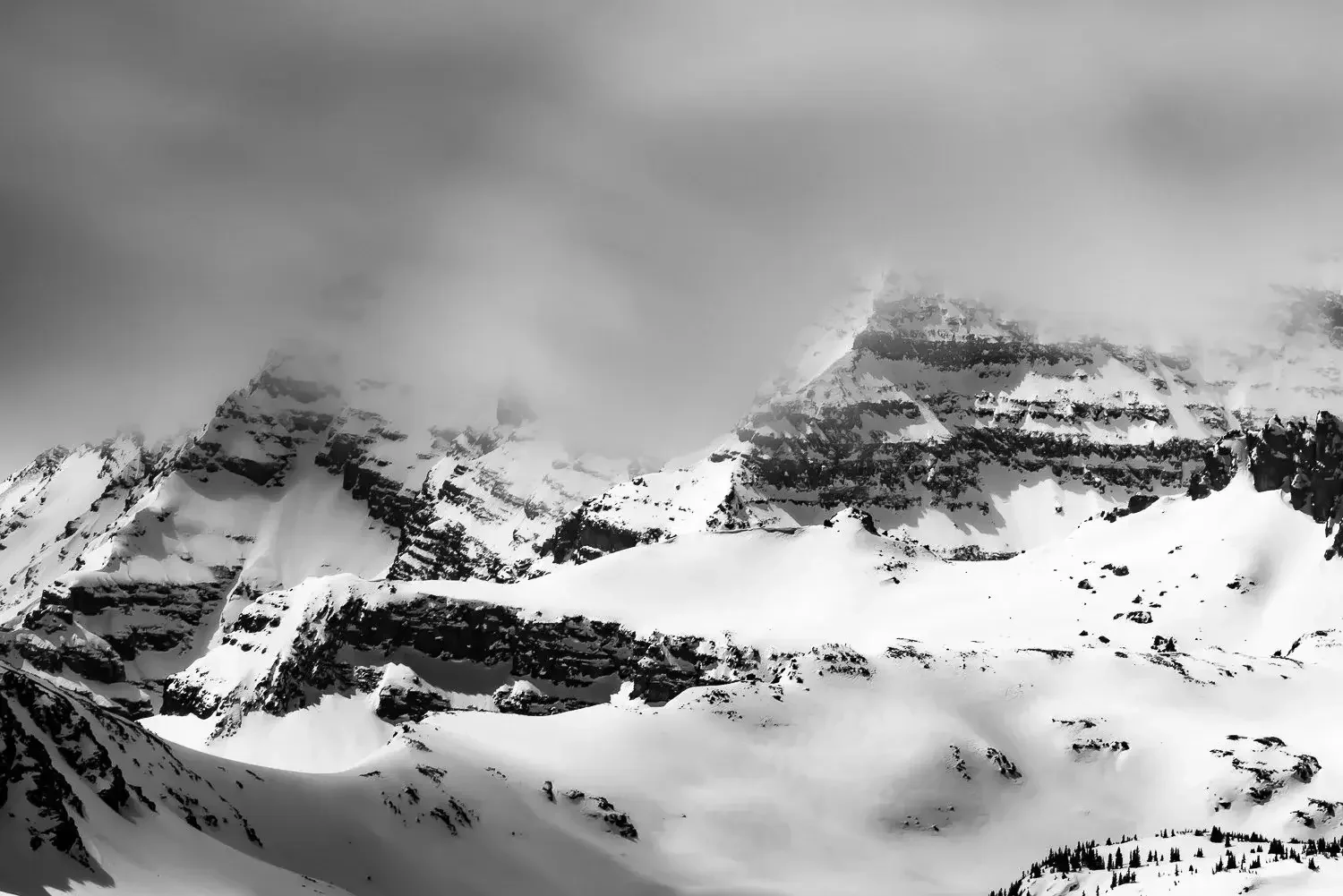 Snow-covered mountain peaks partially obscured by clouds in black and white.