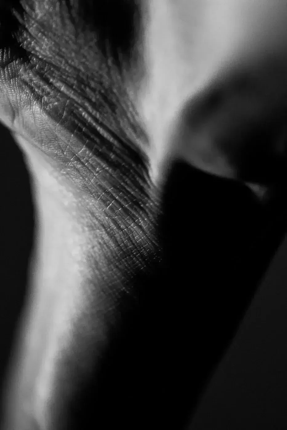 Close-up black and white photograph of a person's face, highlighting textured skin and closed eyes.
