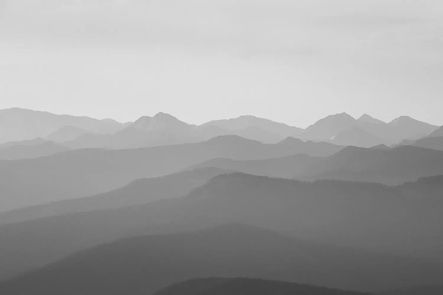 Black and white photo of multiple mountain ranges with fog and clouds, showing a peaceful and expansive landscape.