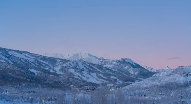 Snow-covered mountains and a small town in a valley under a clear sky at sunset.
