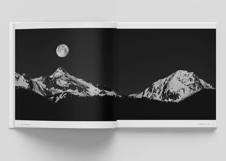 Black and white photograph of snow-covered mountains with a full moon in the night sky.