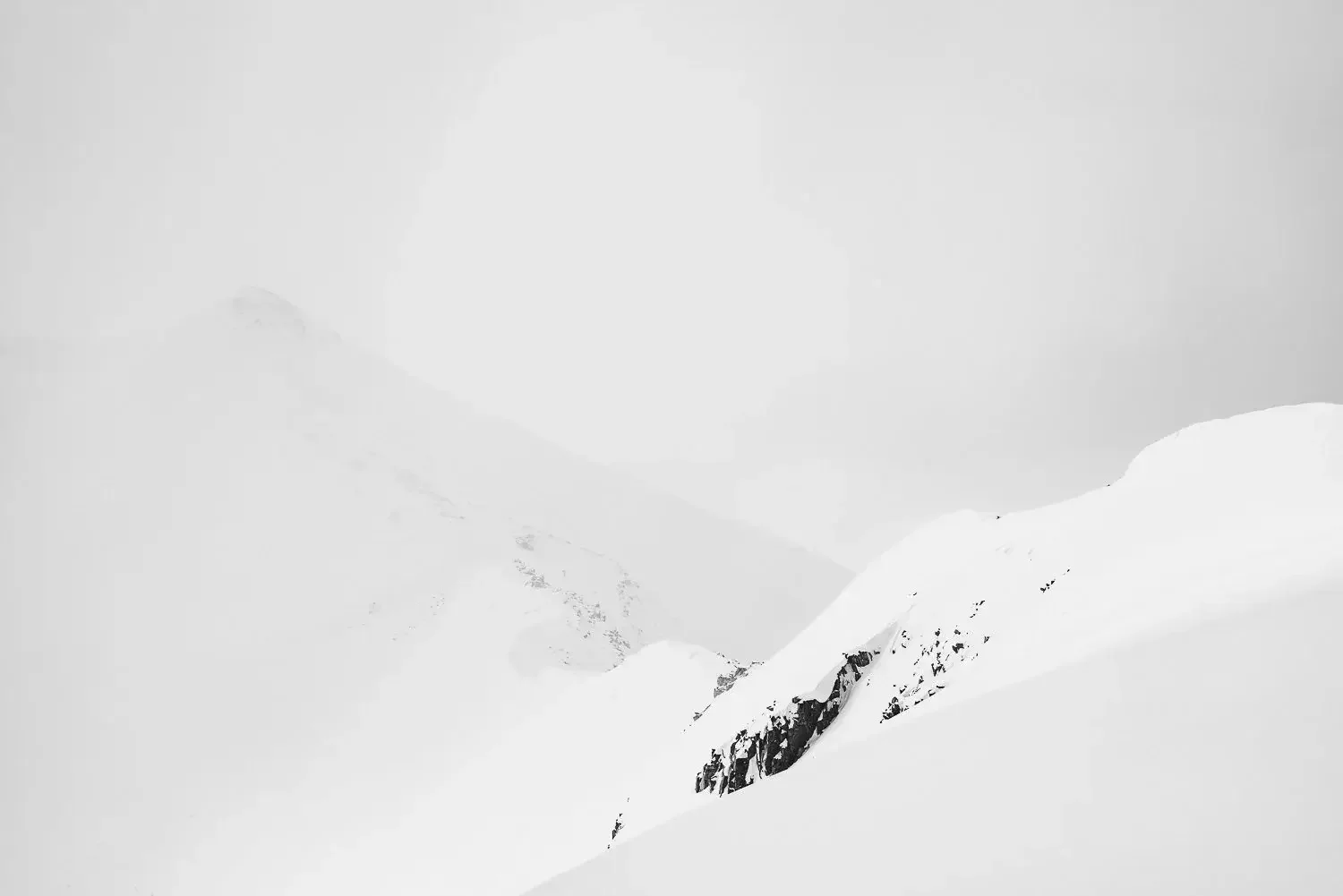 Snow-covered mountain landscape with foggy sky and rocky outcrop.