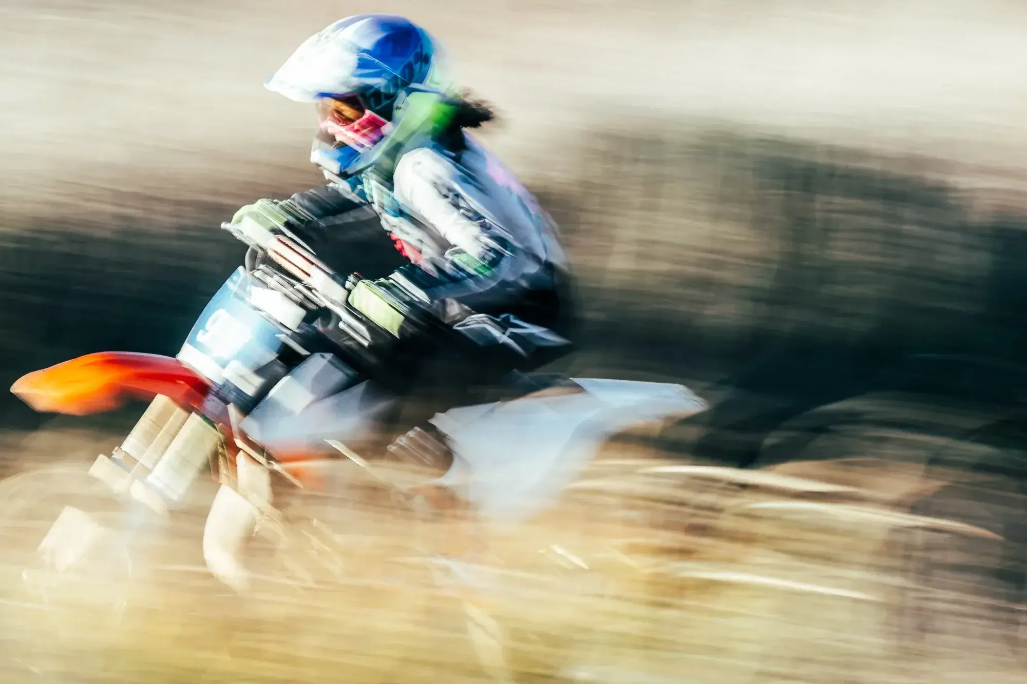 A person riding a dirt bike at high speed through a desert landscape with blurred background and motion blur effects.
