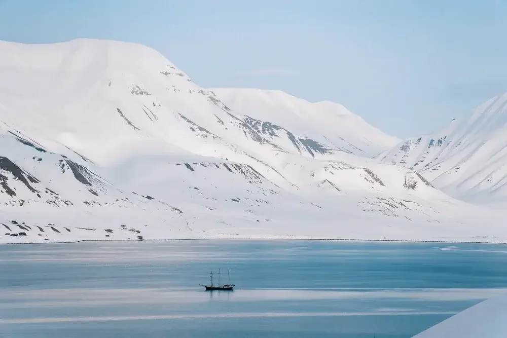 Snow-covered mountains surrounding a body of water with a boat floating on it.
