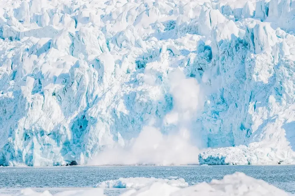 A glacier calving into the ocean, with ice breaking off and splashing into the water.
