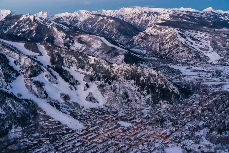Aerial view of a snow-covered mountain town with ski slopes and a surrounding mountainous landscape.
