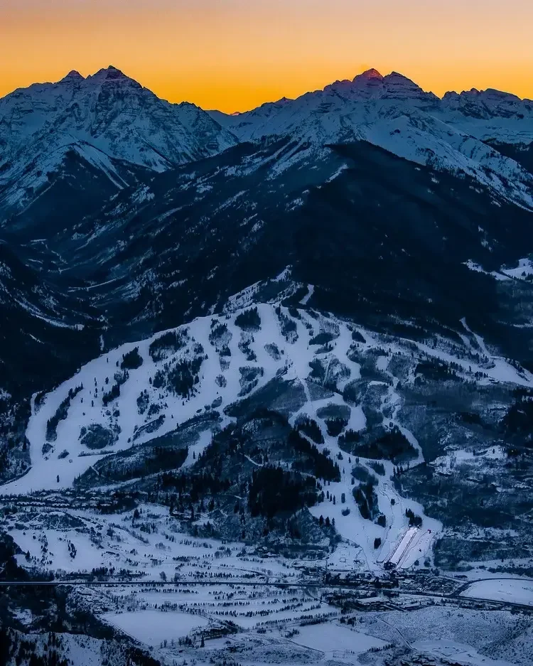 Snow-covered mountain range at sunset with a gradient sky from yellow to blue.
