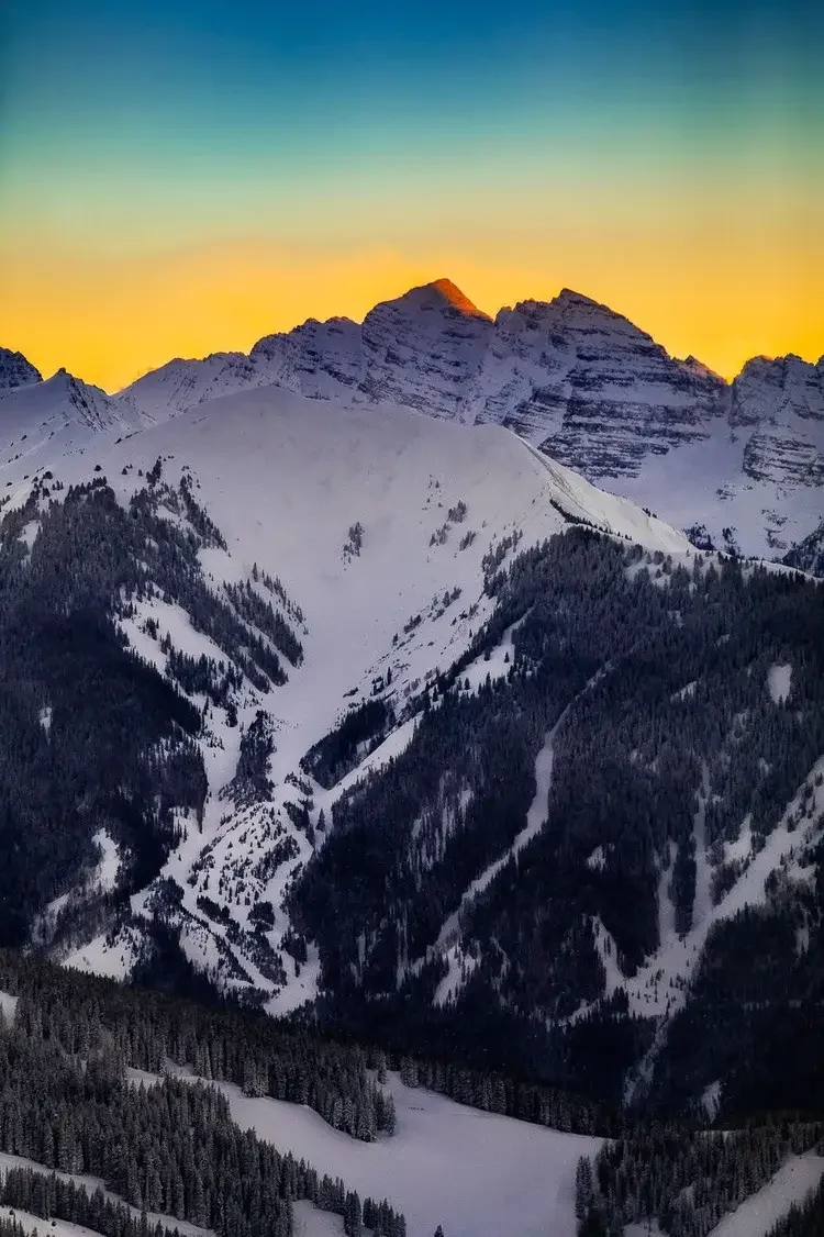 Snow-covered mountains at sunset with a small village and ski slopes in the foreground.
