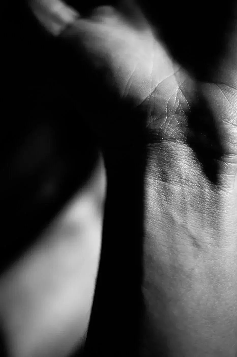 Close-up black and white photo of a person's hand with detailed skin texture, partially shadowed, with a focus on the lines and features of the fingers.
