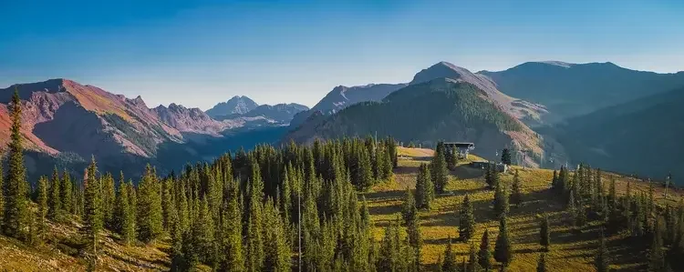 Mountain landscape with pine trees, ski lifts, and clear blue sky
