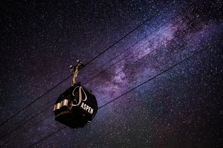 A cable car labeled 'Aspen' against a starry night sky with the Milky Way galaxy visible.
