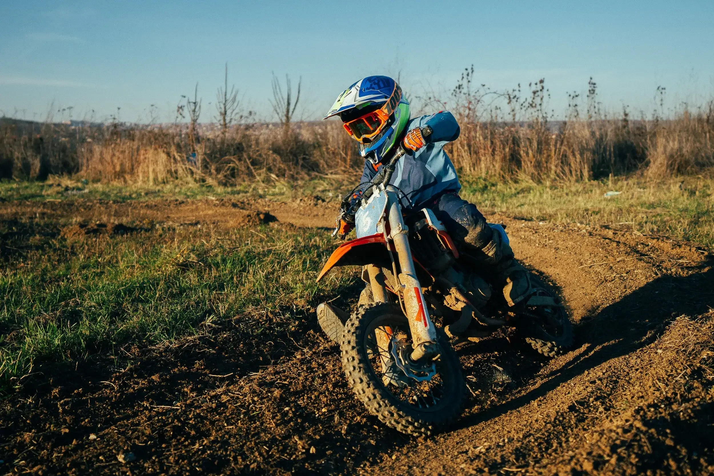 Young child wearing a helmet and protective gear riding a dirt bike on a dirt trail during daytime.
